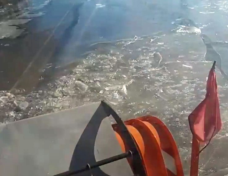 Folyami jégtörőként megy a Közút hókotrója a vízzel elárasztott utakon – videó