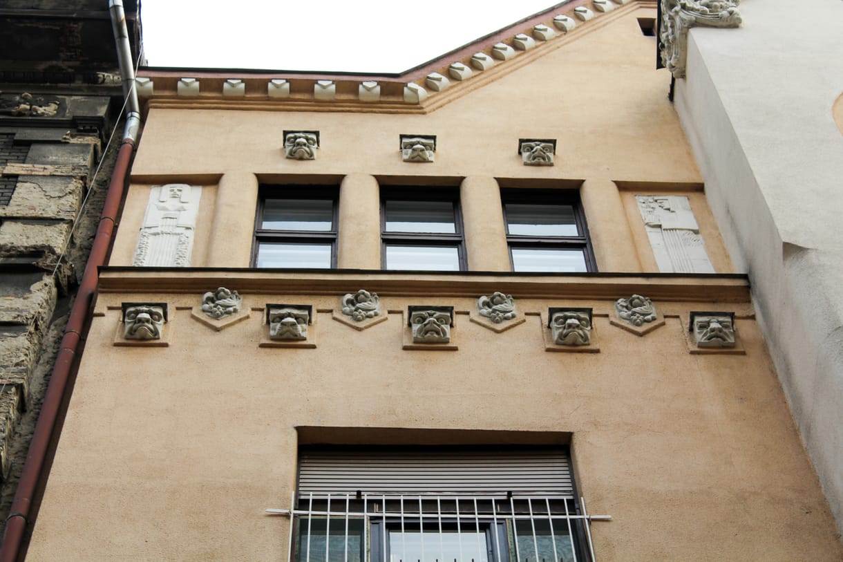 Ők figyelnek minket a homlokzatokról, amikor Budapest utcáin sétálunk