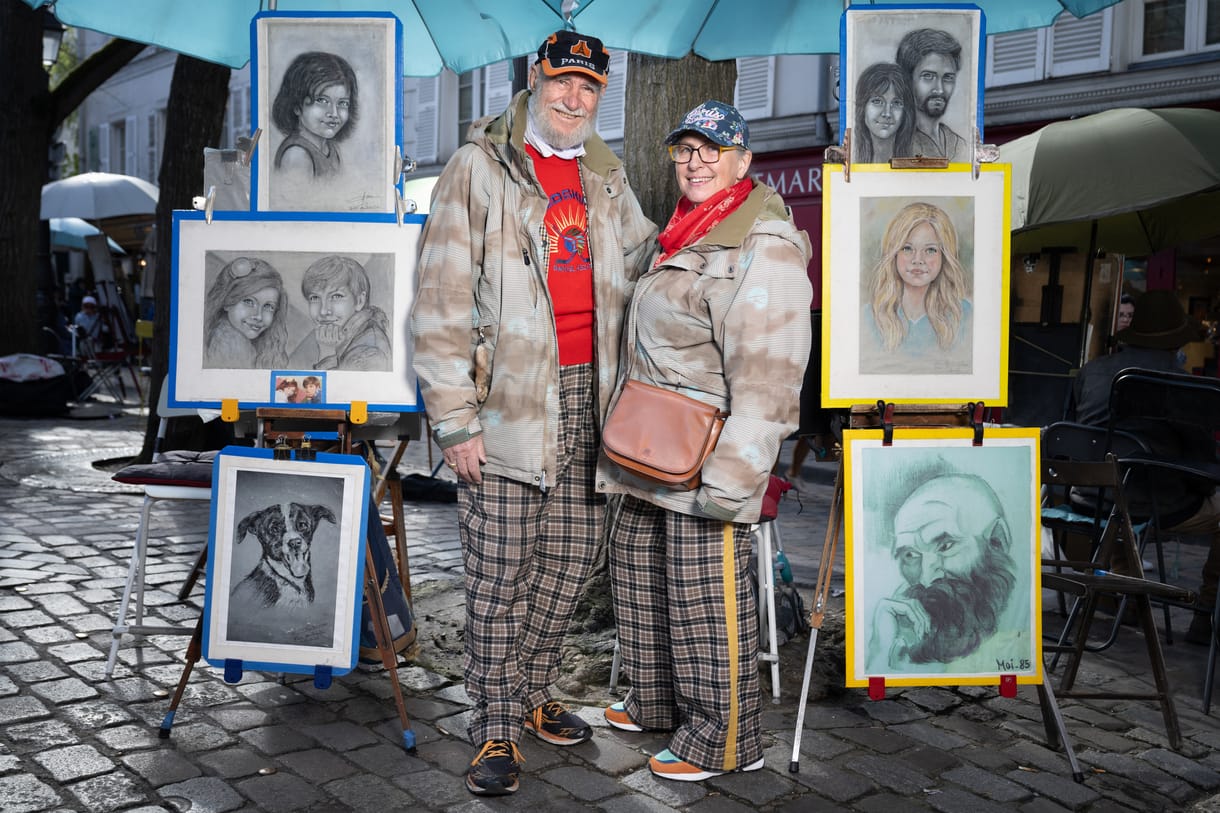 Michel és Claudine művész karikaturisták, akik turisták portréit rajzolják, pózolnak a párizsi Place du Tertre-en 2024. április 10-én.